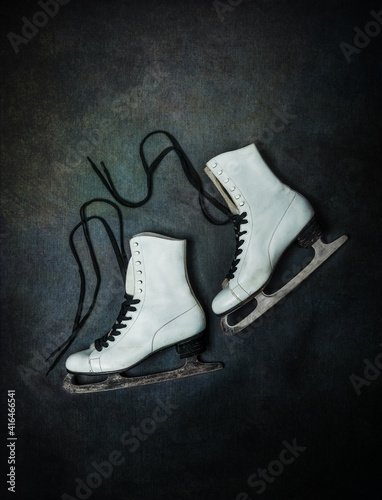 Old white ice skates with black laces on dark rustic background