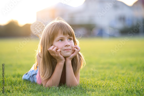 Young pretty child girl laying down on green grass lawn on warm summer day.