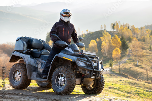 Happy male driver in protective helmet enjoying extreme ride on atv quad motorbike in autumn mountains at sunset.