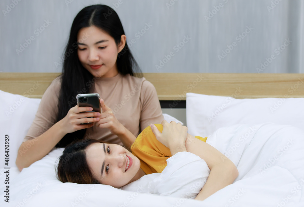 Smiling Two Asian young women Looking at milk in the glass lovely couple on white bed and happy. Funny women Before going to bed . Concept In love homosexual lesbian lgbt, lgbtq, lgbtq+. Smiling Two Asian young women Looking at milk in the glass lovely couple on white bed and happy. Funny women Before going to bed . Concept In love homosexual lesbian lgbt, lgbtq, lgbtq+.