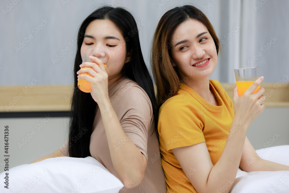 Smiling Two Asian young women looking at orange juice in the glass lovely couple on white bed. Funny women Before going to bed together on cozy. Concept In love homosexual lesbian lgbt, lgbtq, lgbtq+. Smiling Two Asian young women looking at orange juice in the glass lovely couple on white bed. Funny women Before going to bed together on cozy. Concept In love homosexual lesbian lgbt, lgbtq, lgbtq+.