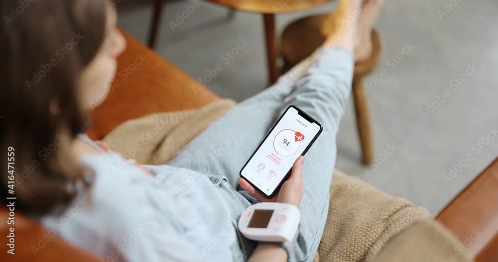 Woman measures heart beat, looking on a smart phone with running health program. Having arrhythmia and high heart rate. Modern gadgets for health monitoring