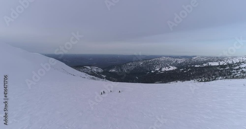 aerial view of a snowmobile. a group of snowmobilers rides in a mountain valley at sunset. A snowmobiler in the Monashees near Revelstoke. 4K ProRes 422 HQ photo