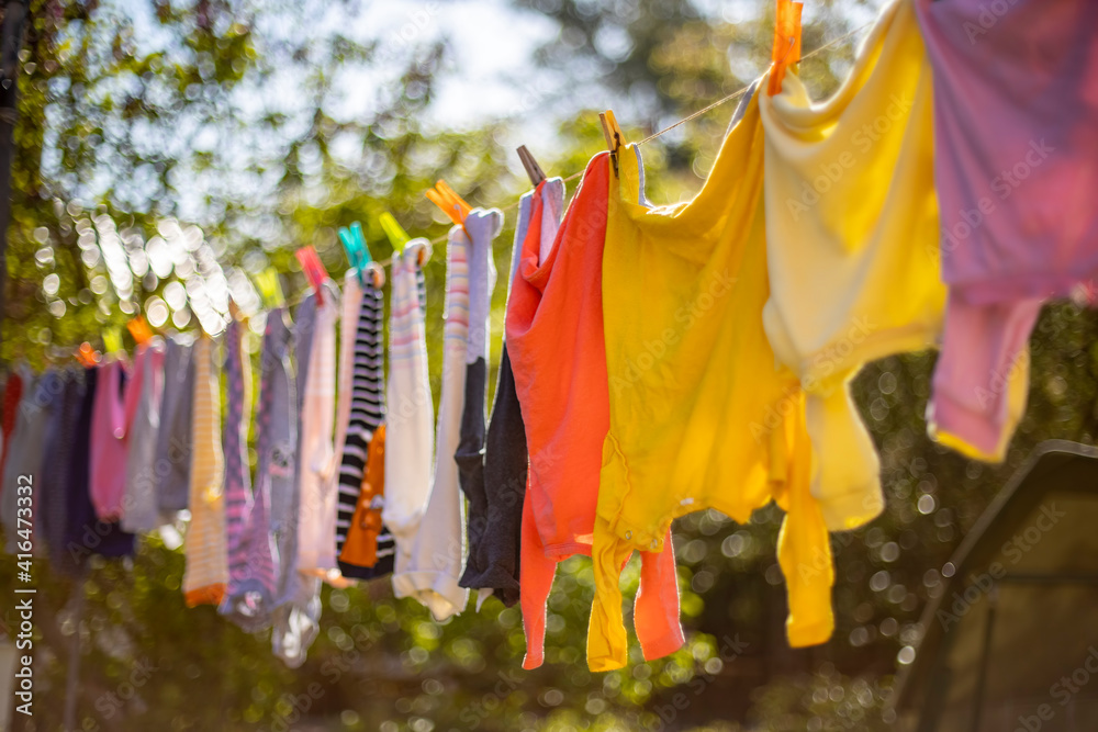 Baby cute clothes hanging on the clothesline outdoor. Child laundry hanging  on line in garden on green background. Baby accessories. Stock Photo