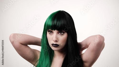 portrait of woman with a green black hair wig straightening long hair on light background