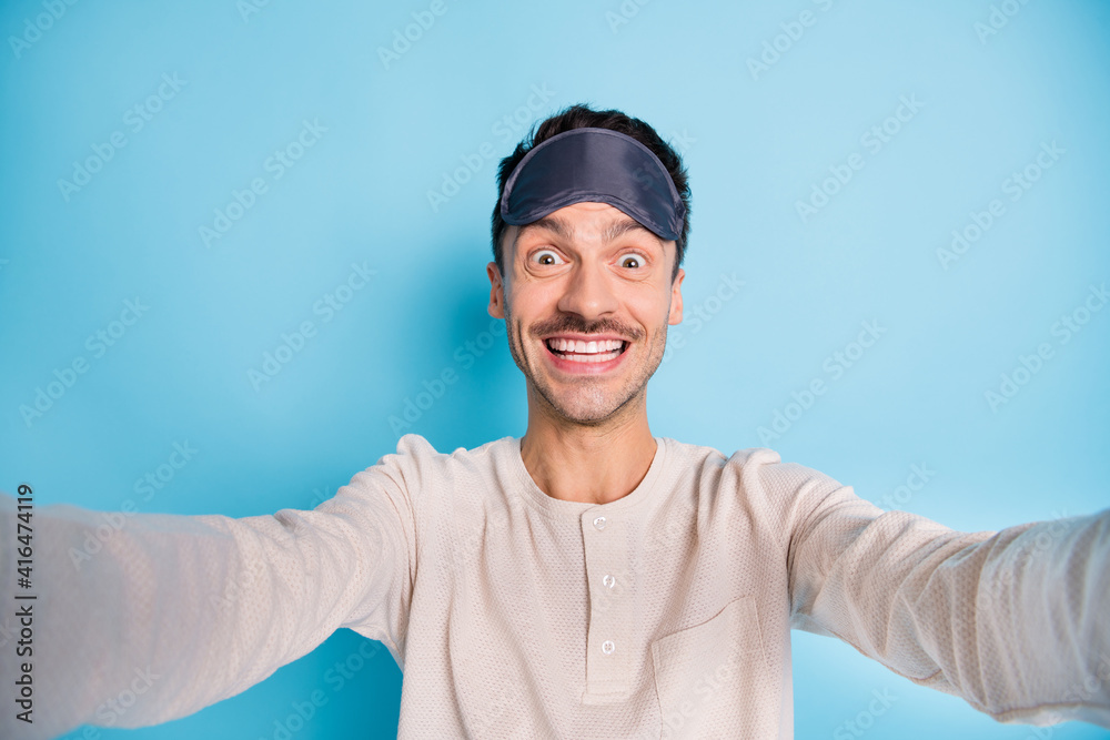 Self-portrait of nice cheerful funny brunet guy wearing sleep mask having fun good mood isolated over bright blue color background Self-portrait of nice cheerful funny brunet guy wearing sleep mask having fun good mood isolated over bright blue color background