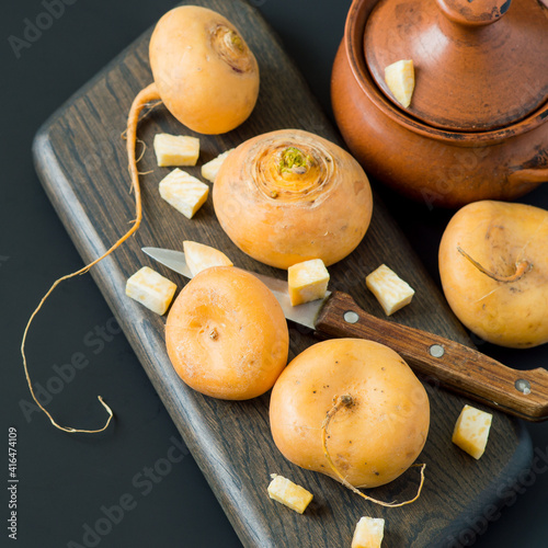 Yellow round turnip on a wooden cutting board, near a small clay pot. Russian kitchen. Selective focus.