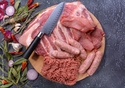 Raw meat products.Barbecue pork ribs, steaks, grilled sausages,minced meat, garnished with spices on a round wooden chopping board.Flat layout.Selective focus.