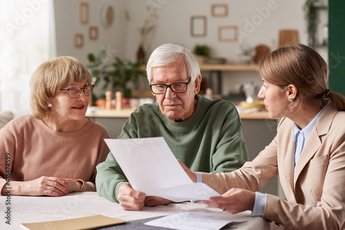 Senior couple sitting at the table and discussing documents with real estate agent they making a will photo