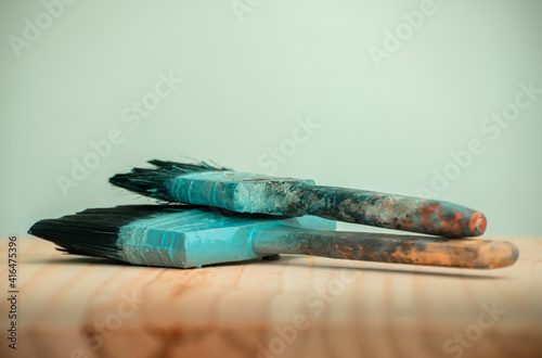 Old two paintbrushes on a wooden table close up view of dirty uncleaned wooden handles, colorful paint stains remain on the handles, Small 2 inch brush on top of a large 5 inch bristle brush.