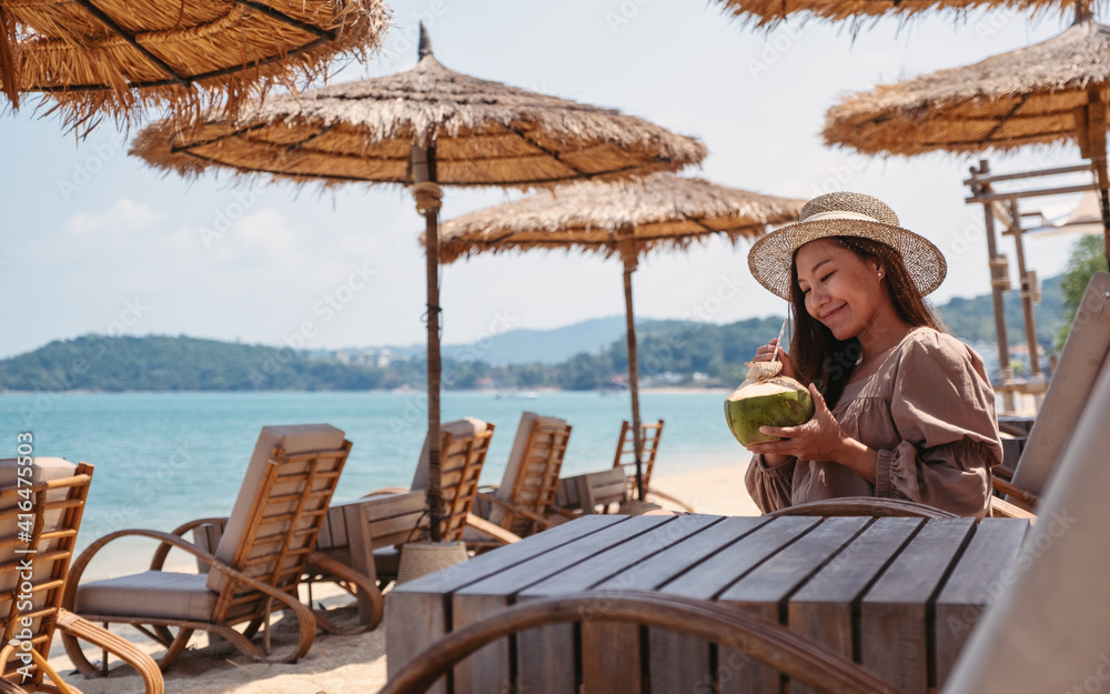 Portrait image of a beautiful young asian woman holding and drinking coconut juice on the beach