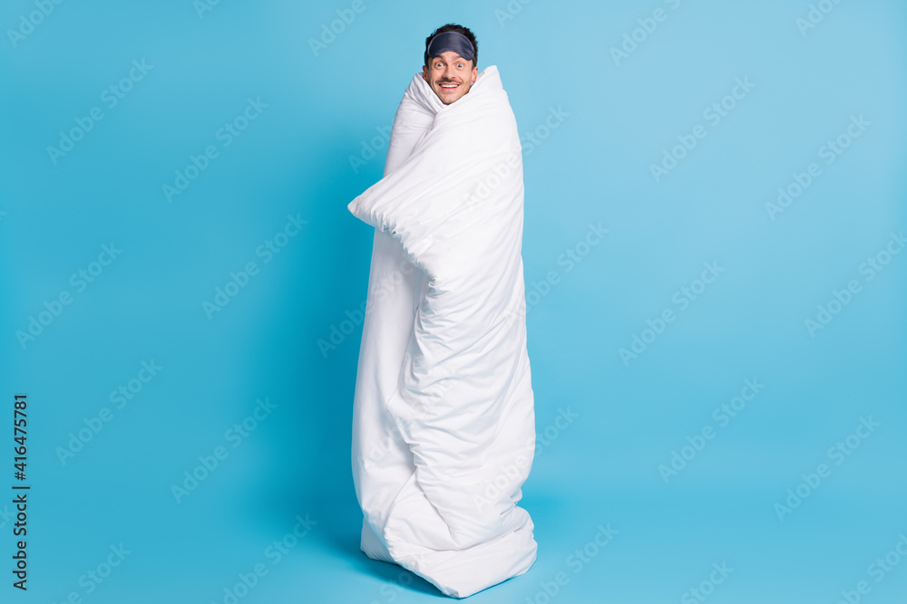 Full length photo portrait of excited smiling man wrapped in blanket isolated on vivid blue colored background Full length photo portrait of excited smiling man wrapped in blanket isolated on vivid blue colored background