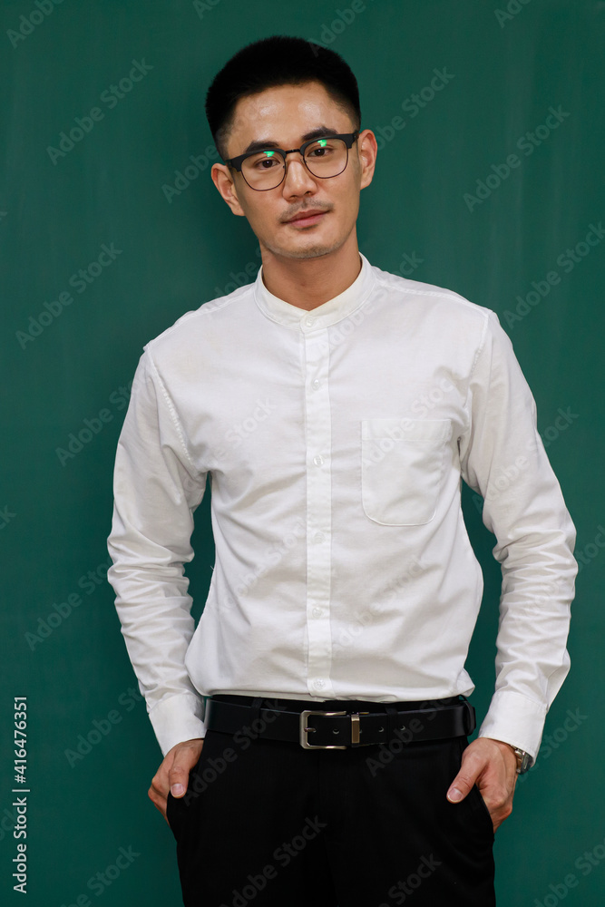 Portrait of young and handsome Asian man wearing eyeglasses and casual business clothes, white shirt and black trousers, standing pose with self-confidence with green background and copy space Portrait of young and handsome Asian man wearing eyeglasses and casual business clothes, white shirt and black trousers, standing pose with self-confidence with green background and copy space