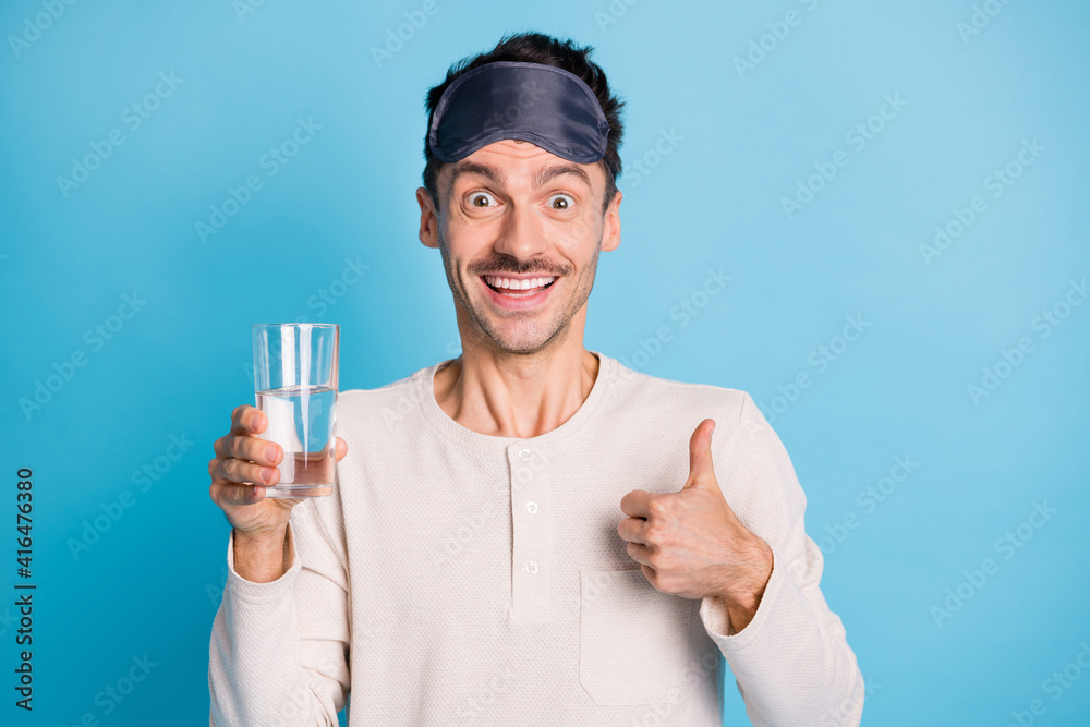 Photo portrait of man holding water glass in one hand showing thumb up isolated on vivid blue colored background Photo portrait of man holding water glass in one hand showing thumb up isolated on vivid blue colored background