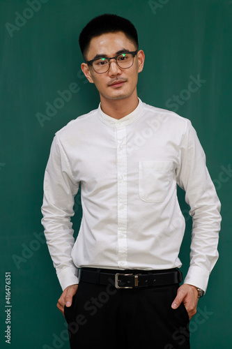 Portrait of young and handsome Asian man wearing eyeglasses and casual business clothes  white shirt and black trousers  standing pose with self-confidence with green background and copy space
