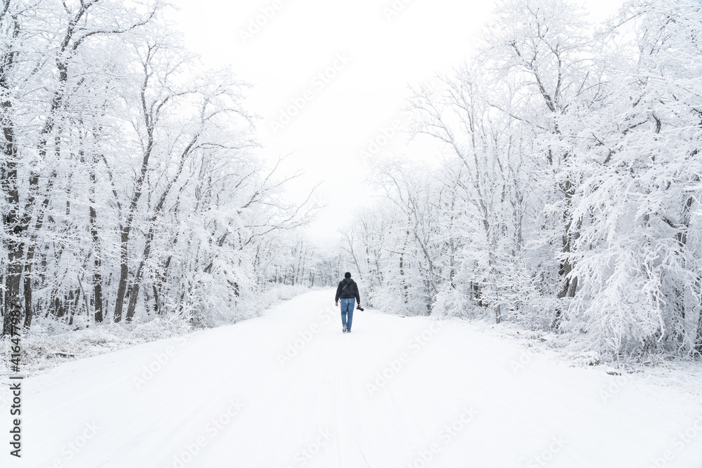 Travel photographer walking on a snowy road in the forest
