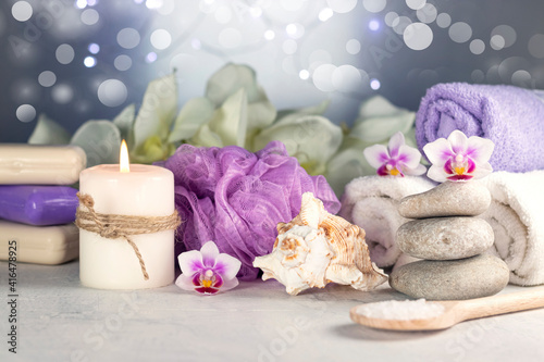 Massage stones, seashell, burning candles, rolled towels, soap, massage oil, sea salt, flowers, abstract lights. Spa resort therapy composition