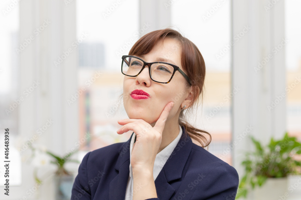 young stylish pretty business woman in a blue jacket and glasses by the window in the office at her workplace is satisfied with the work done young stylish pretty business woman in a blue jacket and glasses by the window in the office at her workplace is satisfied with the work done