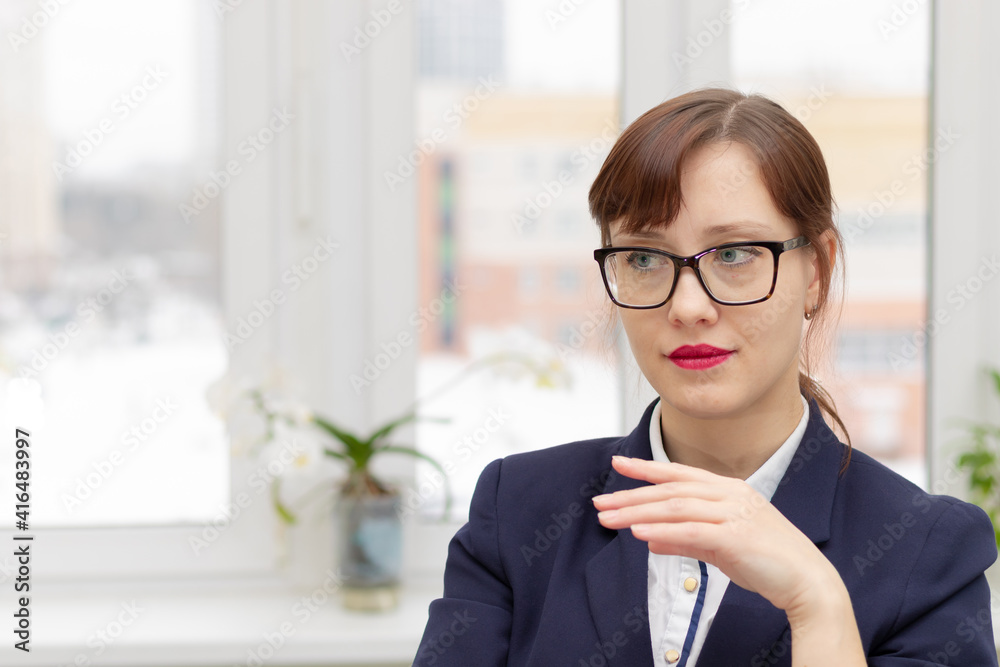 young stylish pretty business woman in a blue jacket and glasses by the window in the office at her workplace is satisfied with the work done young stylish pretty business woman in a blue jacket and glasses by the window in the office at her workplace is satisfied with the work done
