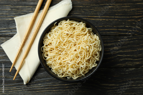 Napkin with chopsticks and bowl with noodles on wooden background