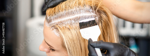 Foto The hairdresser dyeing blonde hair roots with a brush for a young woman in a hai