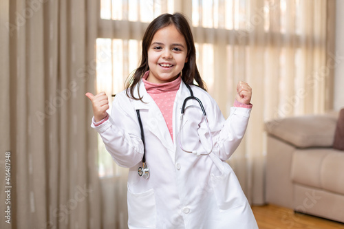 Obraz na plátně Little child dressed in doctor's uniform giving thumbs up in a fun and positive attitude