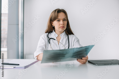 Young caucasian woman doctor wearing white medical coat and stethoscope holds the x-ray. Coronavirus diagnosis