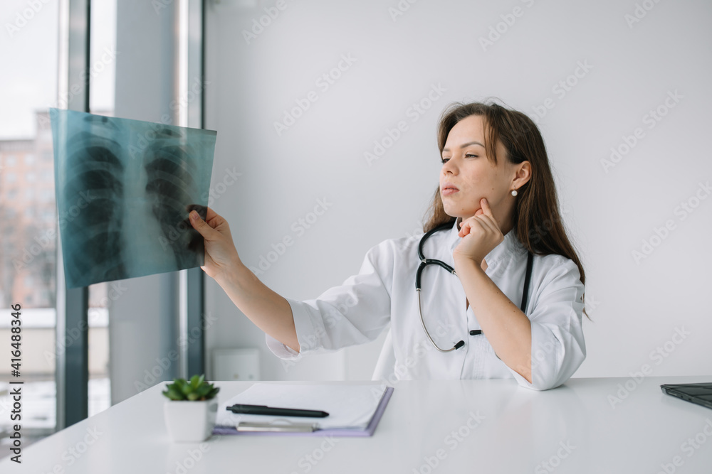 Young caucasian woman doctor wearing white medical coat and stethoscope holds the x-ray in the hospital. Medicine concept Young caucasian woman doctor wearing white medical coat and stethoscope holds the x-ray in the hospital. Medicine concept