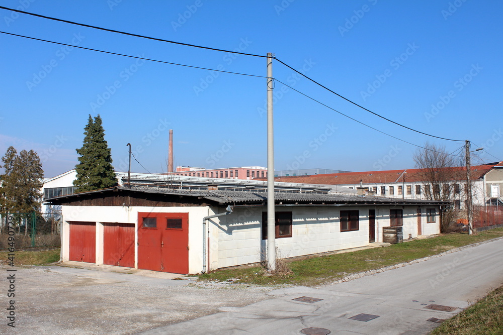 Elongated white garage and storage building in old industrial part of town surrounded with cracked paved street and factory buildings in background on warm sunny winter day