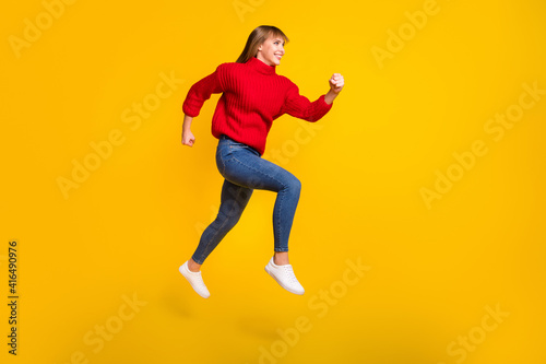 Full size profile photo of blond optimistic lady jump wear red sweater jeans sneakers isolated on bright yellow color background © deagreez
