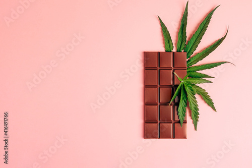 Dark chocolate and cannabis cannabis leaf on pink background. Horizontal frame copy space top view.