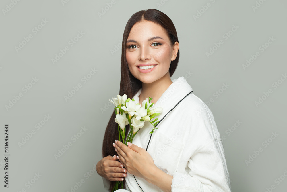 Attractive woman brunette after bath holding white flowers and smiling on white. Skincare and facial treatment concept Attractive woman brunette after bath holding white flowers and smiling on white. Skincare and facial treatment concept