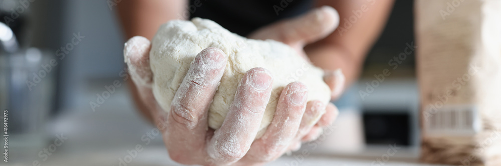 Man's hand holds the dough over table where flour is scattered. Cooking dough products at home concept Man's hand holds the dough over table where flour is scattered. Cooking dough products at home concept