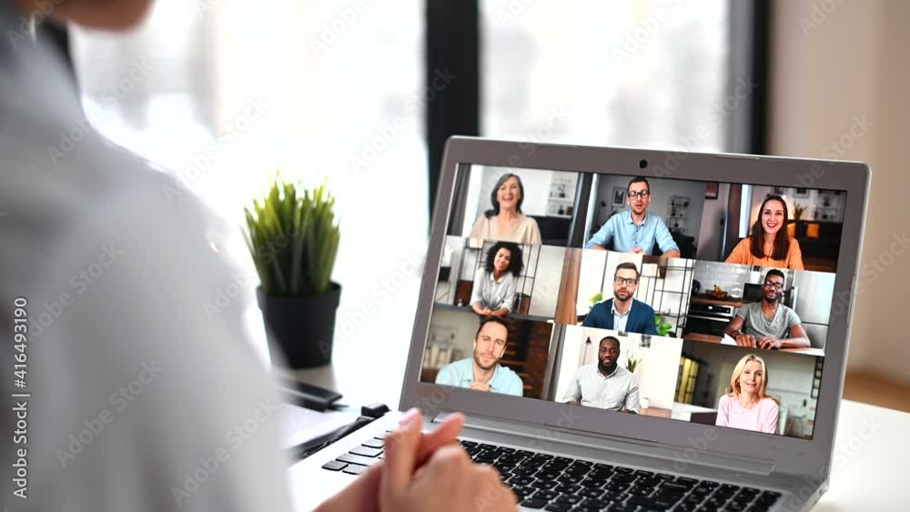 Back view of mixed-race woman waving at the laptop screen with people profiles, using an application for distance video communication with coworkers, webinar participants, meeting online in pandemic