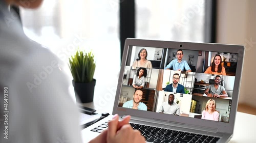 Back view of mixed-race woman waving at the laptop screen with people profiles, using an application for distance video communication with coworkers, webinar participants, meeting online in pandemic