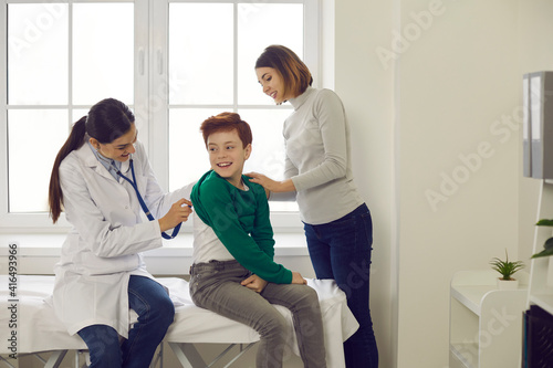 Mother and happy child visiting doctor. Smiling pediatrician or family practitioner checking little patient's lungs, listening to boy's breath through stethoscope during check-up at clinic or hospital