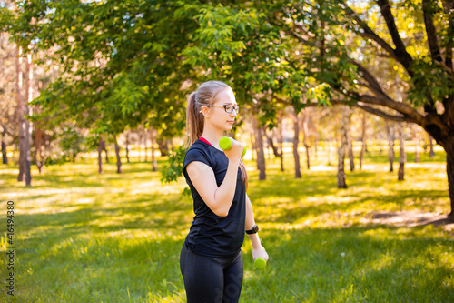 Young woman doing exercise with dumbbells. Healthy lifestyle concept. Sports training in the park.