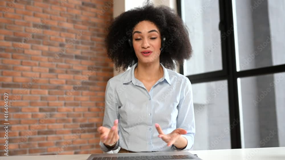 Video chat with a friendly young mixed-race woman with Afro hairstyle in headset, female worker in emergency helpline or in the customer service department as call center operator, talking at camera
