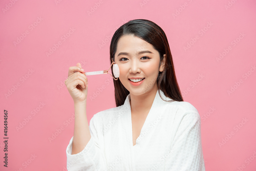 Beautiful young woman with perfect skin using a rose quartz face roller with natural quartz stones Beautiful young woman with perfect skin using a rose quartz face roller with natural quartz stones