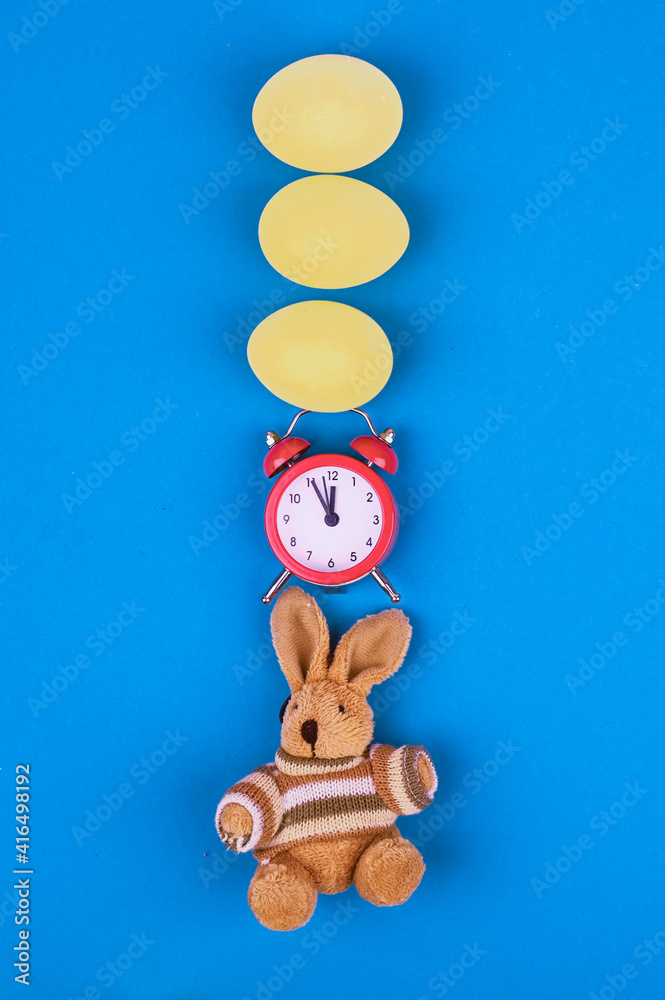 Obraz premium Easter concept with alarm clock, bunny toy and eggs on light blue background.