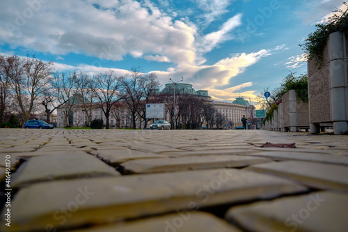 Center of Sofia Bulgaria. Photo taken from low angle of yellow cobblestones with cars and sun rising sky background. Bulgaria. Sofia. 06.01.2021 photo