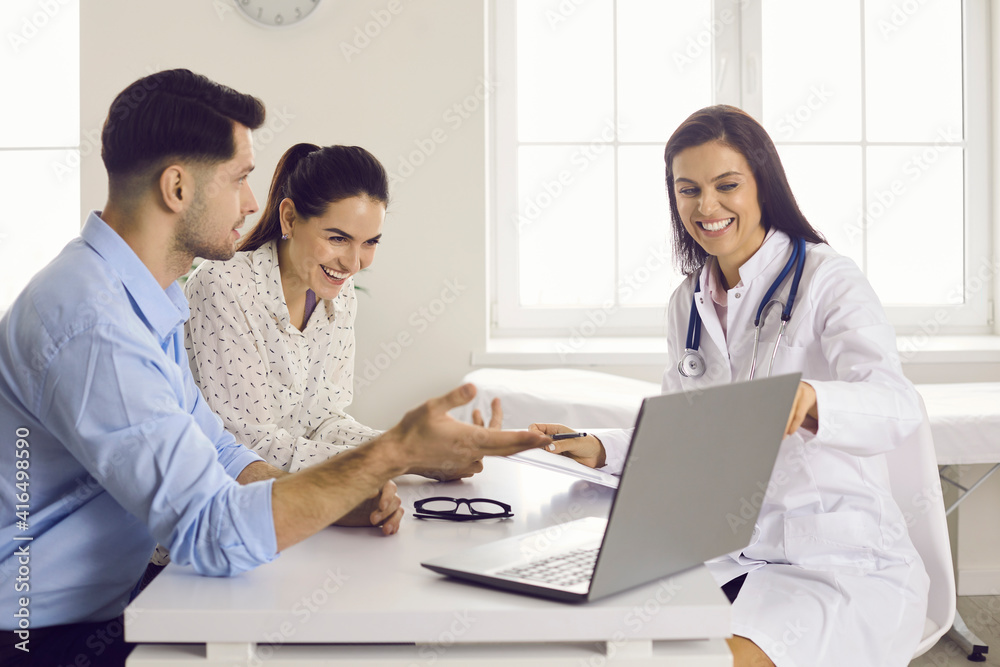 Expecting a baby. Smiling nurse showing scan picture to future parents. Happy couple, husband and his pregnant wife, looking at ultrasound image on computer screen sitting at table at doctor's office Expecting a baby. Smiling nurse showing scan picture to future parents. Happy couple, husband and his pregnant wife, looking at ultrasound image on computer screen sitting at table at doctor's office