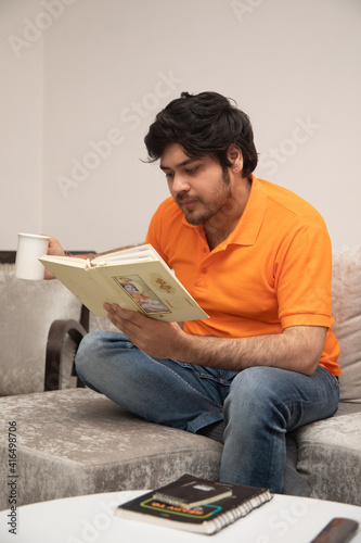 Asian Indian man gaming, streaming and watching TV alone in living room on a grey sofa and white table