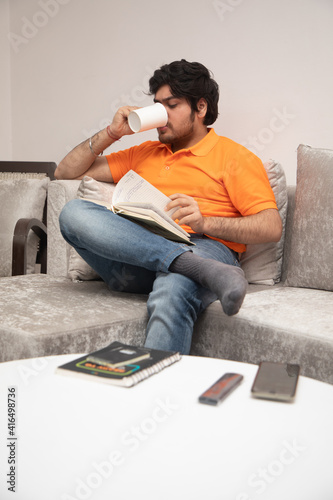 Asian Indian man gaming, streaming and watching TV alone in living room on a grey sofa and white table