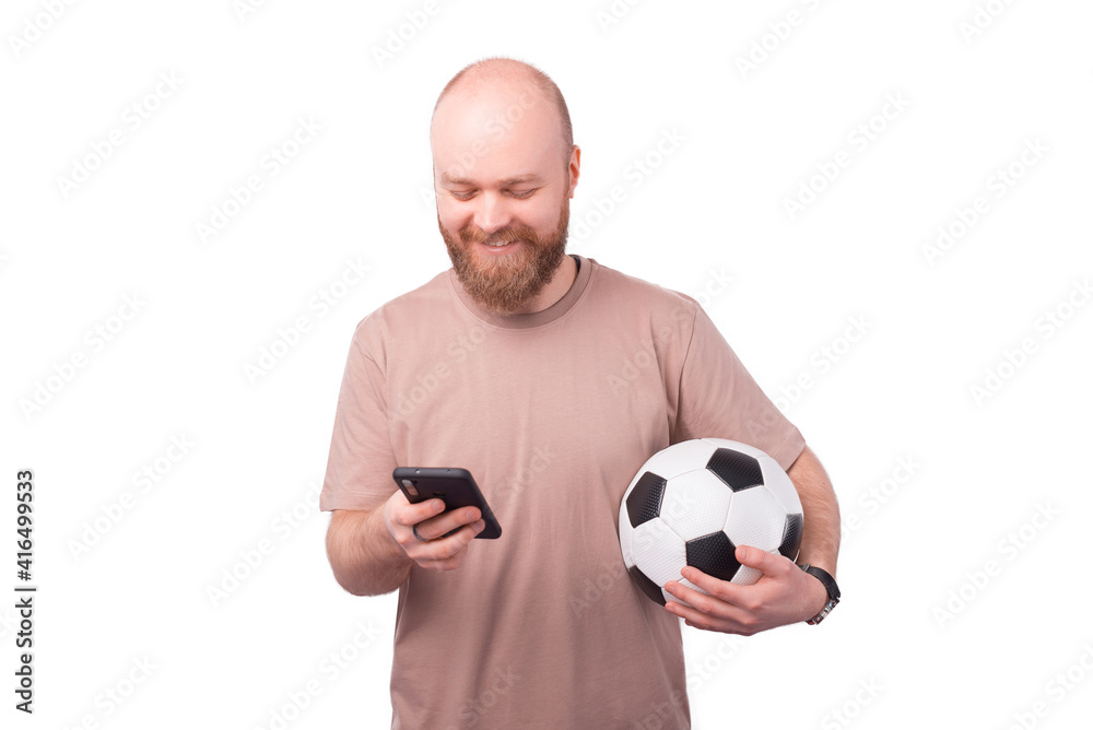 happy young bearded man using smartphone and holding soccer ball