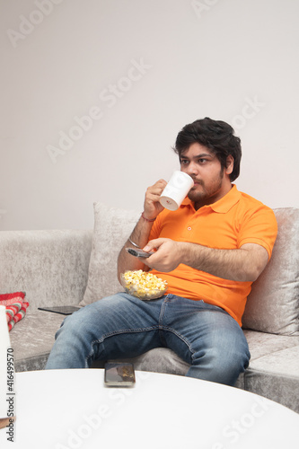 Asian Indian man gaming, streaming and watching TV alone in living room on a grey sofa and white table
