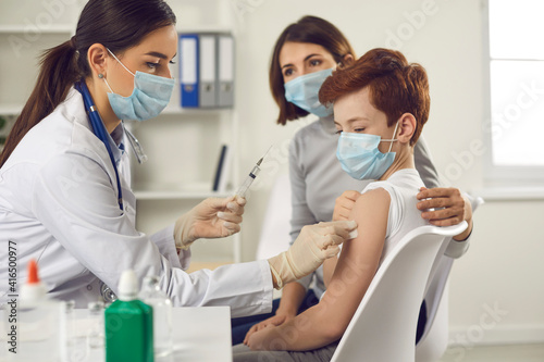 Vaccination and immunization for children concept. Child getting flu or Covid-19 shot at the hospital. Nurse in medical face mask giving injection to little boy who came to the doctor's with mother