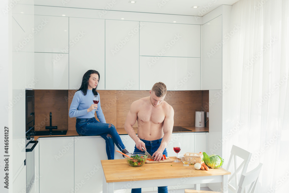 Obraz premium Athlete husband prepares lunch from vegetables to his wife, spend free time together in the kitchen