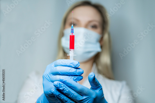 Young doctor with mask and gloves is holding a syringe with blood for tests