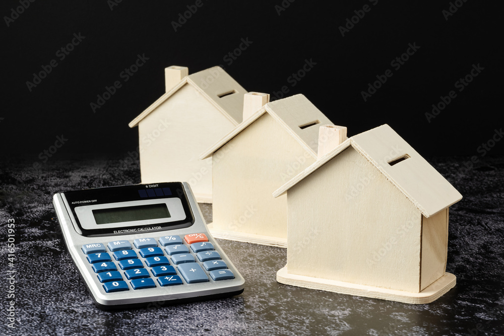Calculator and three house-shaped wooden piggy banks. dark background and dark tile surface. suitable for the concept of financing or savings for housing or real estate Calculator and three house-shaped wooden piggy banks. dark background and dark tile surface. suitable for the concept of financing or savings for housing or real estate